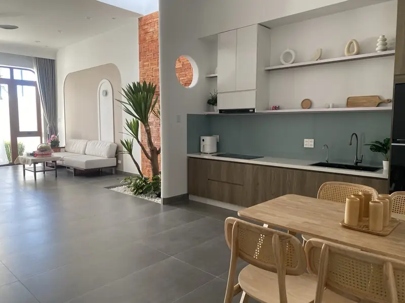 Bếp và bàn ăn nhà cấp 4 B-House Kon Tum — tủ gỗ, kính ốp xanh, ghế mây
