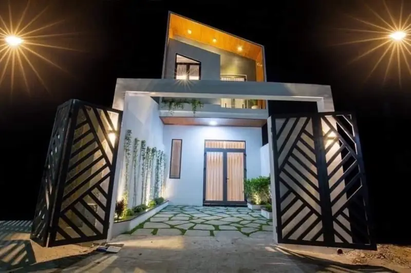 Mặt tiền nhà phố 2 tầng CP-House 6x20 Kon Tum đêm — cổng sắt họa tiết, sân đá hộc, khối trắng mái gỗ