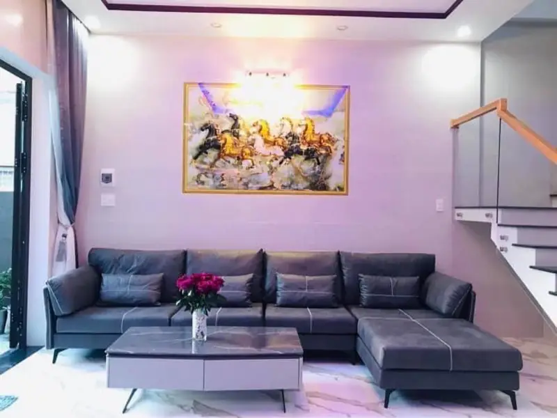 Phòng khách nhà phố 2 tầng hiện đại Kon Tum — sofa xám chữ L, tranh, cầu thang kính tay vịn gỗ