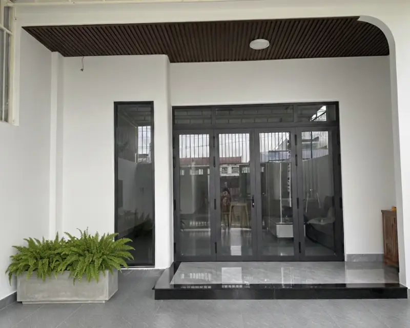 Hiên nhà phố hiện đại Kon Tum — cửa nhôm kính đen xếp, trần nan gỗ, chậu dương xỉ