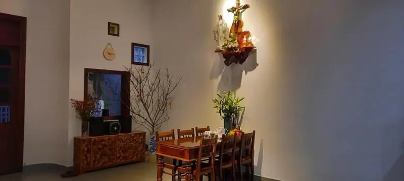 Phòng ăn nhà cấp 4 HQ-House Kon Tum — bàn gỗ, bàn thờ Công giáo trên tường