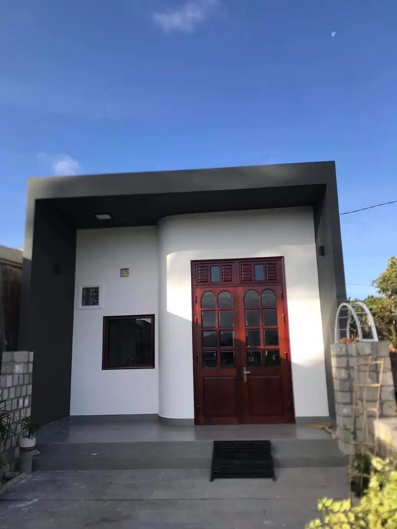 Mặt tiền nhà cấp 4 HQ-House 5x20 Kon Tum — khung xám, tường trắng, cửa gỗ kính hai cánh